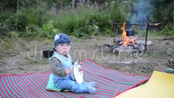 可爱的孩子坐在篝火旁玩盘子和勺子视频的预览图