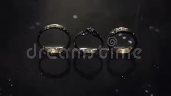 婚礼戒指和订婚戒指躺在黑暗的水面上用光线照亮宏观水溅了雨水视频的预览图