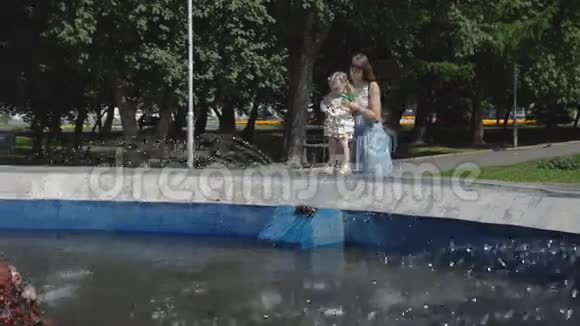 小女孩在妈妈的支持下把手伸进喷泉里视频的预览图