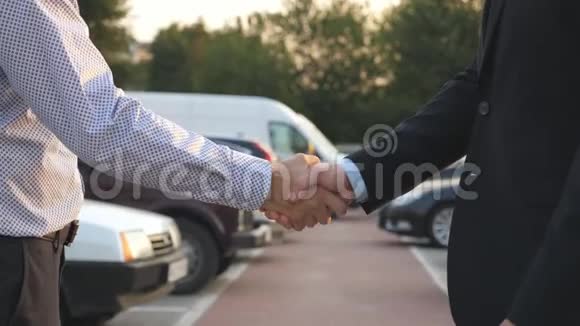 两个商人互相握手车停在后台经理或经销商之间的握手视频的预览图