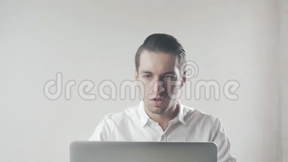 穿着白色衬衫的年轻人非常高兴坐在办公室的笔记本电脑旁视频的预览图