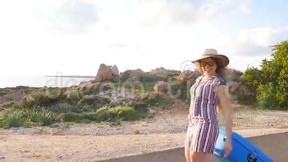 戴帽子的年轻女旅行者带着蓝色的手提箱跑视频的预览图