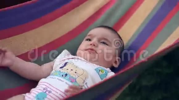 美丽快乐的小女孩躺在花园的吊床上笑视频的预览图