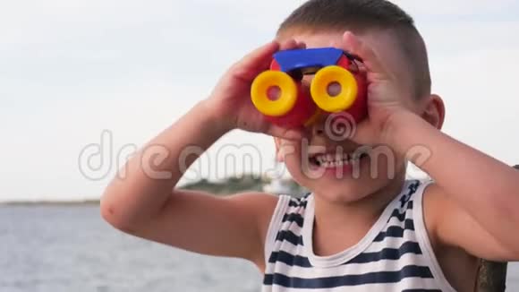 快乐的小男孩穿着背心和太阳镜坐在天空背景的防波堤上视频的预览图