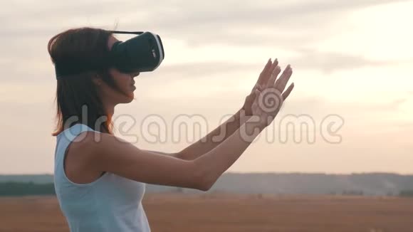 日落时在野外的虚拟现实护目镜中的女孩女人看着太阳的虚拟现实眼镜视频的预览图