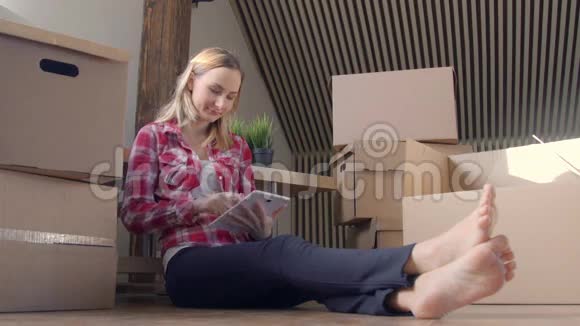 年轻女子在新家坐在地板上时使用平板电脑视频的预览图