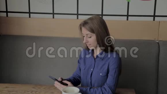 一个漂亮的女孩坐在咖啡馆里拿着电话喝咖啡视频的预览图
