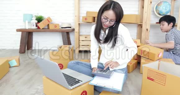 年轻的亚洲妇女带着一个男孩在泰国工作并在泰国邮政信箱中打包视频的预览图