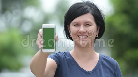 快乐美丽的女人在户外展示电话视频的预览图