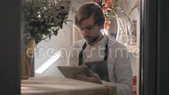 现代花店在工作场所用平板电脑在冰箱接电话订购的英俊胡子花店视频的预览图