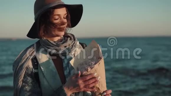 秋海背景下戴着帽子和外套的可爱迷人女人的肖像带着花束的年轻女子视频的预览图