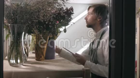 现代花店在工作场所用平板电脑在冰箱接电话订购的英俊胡子花店视频的预览图