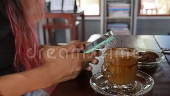 混合种族亚洲妇女与彩色头发使用移动应用程序智能手机在咖啡厅喝咖啡和短信高清高清视频的预览图