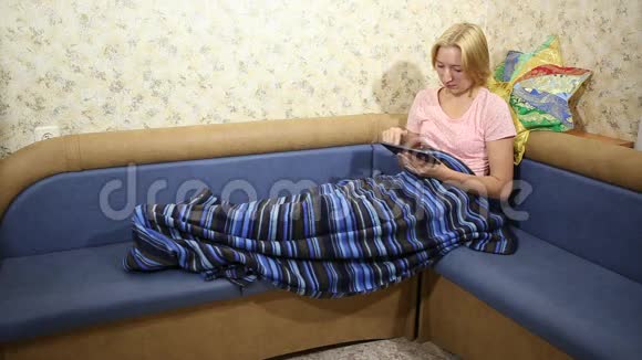 年轻的lass坐在沙发上在平板电脑上的社交网络上阅读帖子视频的预览图