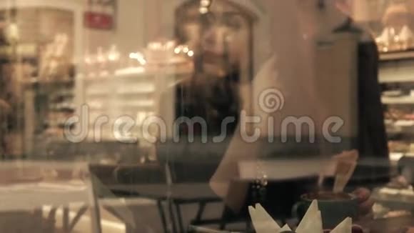 美丽的黑发女孩在糕点店喝热巧克力从外面透过窗户观看4K视频视频的预览图
