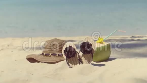 女帽拖鞋和椰子孤独地躺在海边的沙滩上视频的预览图