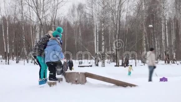 在冬天的公园里下雪时女孩帮助她的弟弟在原木上跑步视频的预览图