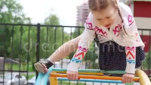 穿着衣服的小女孩在夏天爬上孩子们的操场视频的预览图