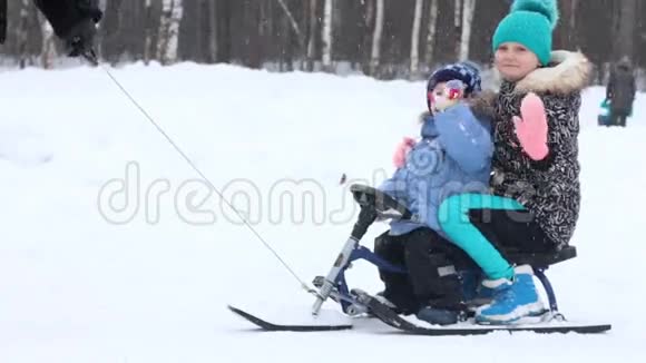 快乐的男孩和女孩骑在雪橇上在公园下雪时挥手视频的预览图
