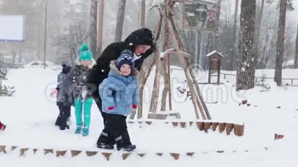 冬天的公园里下雪时两个孩子和一个男人在附近玩耍视频的预览图