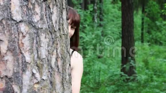 在绿色的夏日森林里漂亮的女人从树后偷看视频的预览图
