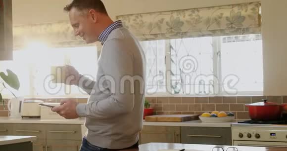 男子在厨房喝咖啡时使用手机视频的预览图