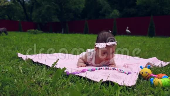 美丽的小女孩躺在花园里的粉红色毯子上肚子上的草上视频的预览图