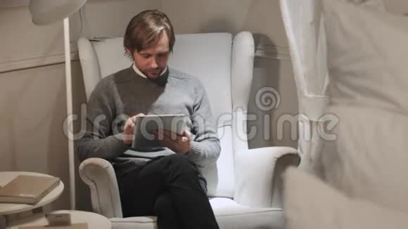 带数字平板电脑的人自信的年轻帅哥拿着数码平板电脑坐在大房间里微笑着视频的预览图