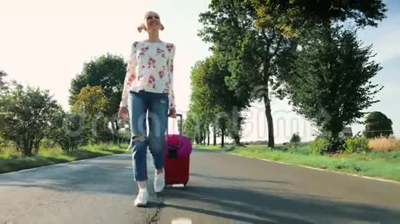 开朗的年轻女士带着手提箱在路上行走视频的预览图