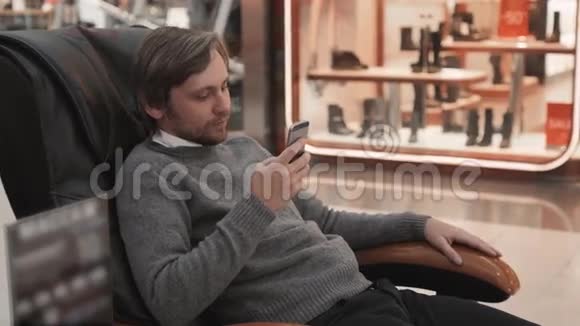 商场里的男人躺在按摩椅上近距离拍摄使用智能手机视频的预览图
