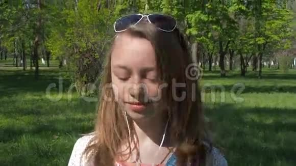 戴着耳机的少女戴墨镜和带着手机听音乐的女孩公园里阳光明媚的一天视频的预览图