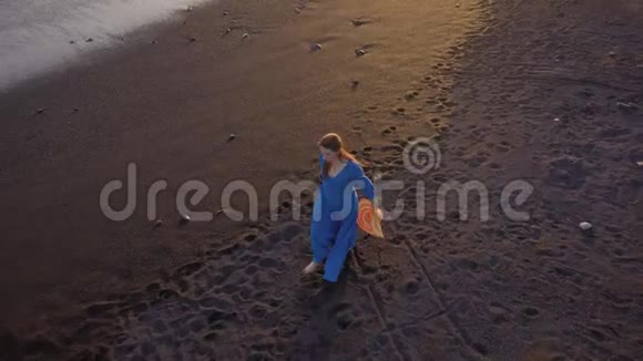鸟瞰一个穿着蓝色连衣裙的女孩在沙滩上用黑色的沙子行走西班牙加那利群岛特内里费视频的预览图