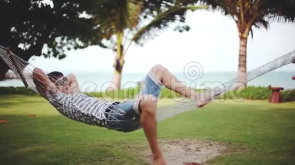 戴太阳镜的年轻人在美丽的热带海滩上的吊床上放松假期概念1920x1080视频的预览图