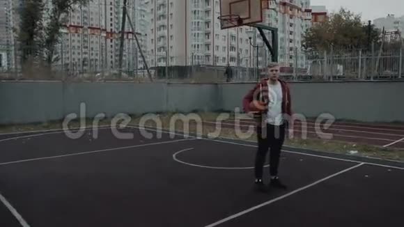 年轻人维塔拿着篮子球看着球场上室外的摄像机视频的预览图