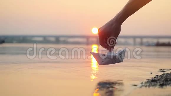 人的手把纸船放在水面上在美丽的日落时分把它推开阳光在海里反射视频的预览图