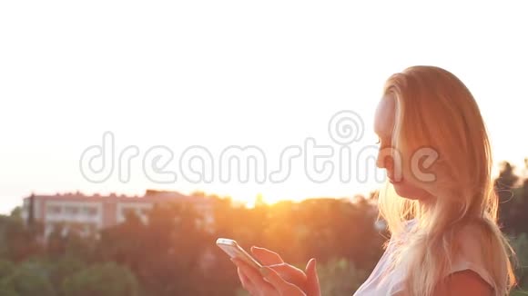 女孩在日落时在海边使用智能手机慢动作视频的预览图