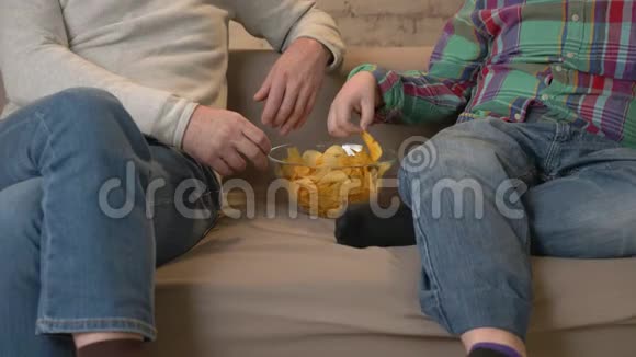 祖父和孙子坐在沙发上看电视吃薯片家庭舒适家庭闲适温馨视频的预览图