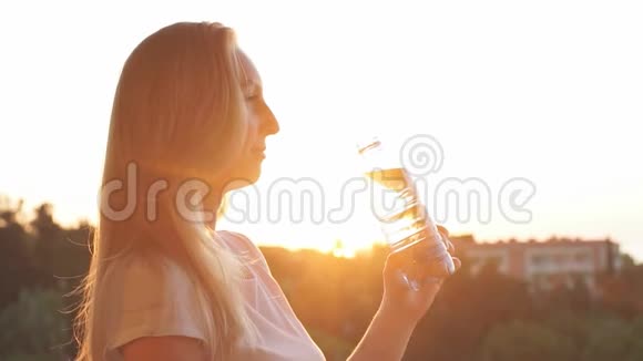 年轻女子在日落时从瓶子里喝水动作缓慢视频的预览图