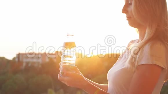 年轻女子在日落时从瓶子里喝水动作缓慢视频的预览图