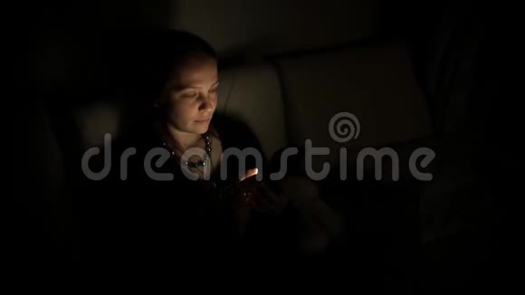 一位中年白种人妇女晚上坐在沙发上的房间里用智能手机与朋友交流视频的预览图