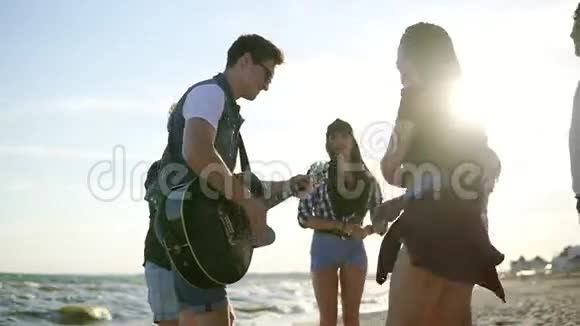 海滩上的夏季派对年轻的朋友喝鸡尾酒在圆圈里跳舞弹吉他唱歌和视频的预览图