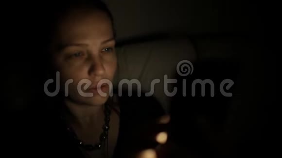 一位中年白种人妇女晚上坐在沙发上的房间里用智能手机与朋友交流视频的预览图