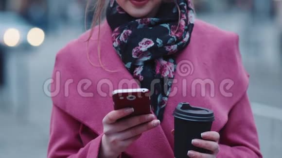 迷人的年轻女孩随意剪发拿着一杯热咖啡用手机发短信然后看上去视频的预览图