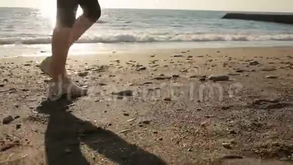 女人穿着跑鞋的腿沿着海滨海洋奔跑在海边奔跑视频的预览图
