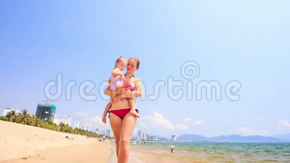 金发女郎母亲挽着女儿沿着潮湿的沙滩视频的预览图