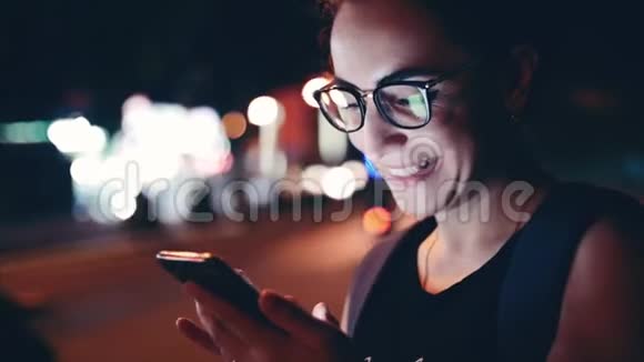 在一个夜晚的城市里漂亮的女人一边用手机在街上行走在后台可以看到视频的预览图