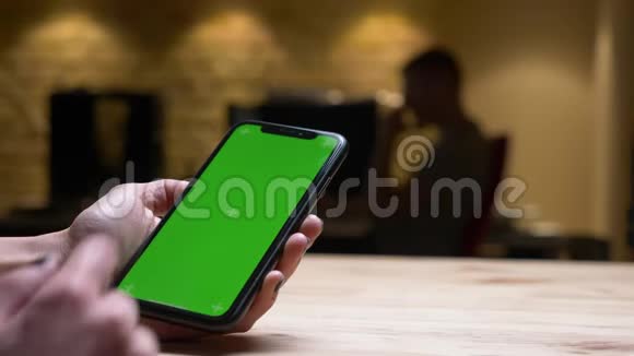 室内办公室中女性手拿绿色屏幕手机的特写后景拍摄视频的预览图