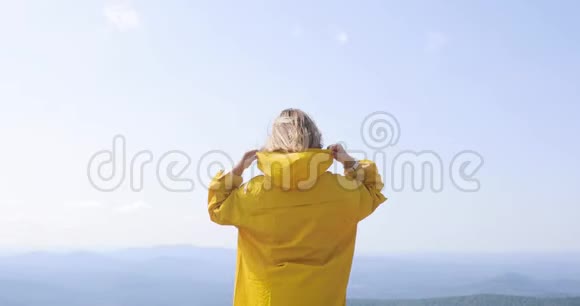 穿着黄色雨衣的白种人女徒步旅行者站在山顶视频的预览图