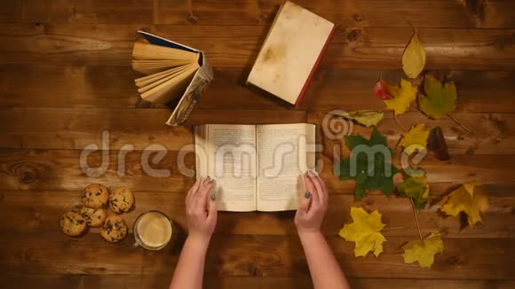 秋季概念俯视图书枫叶烤旧的木桌女人翻阅书页视频的预览图