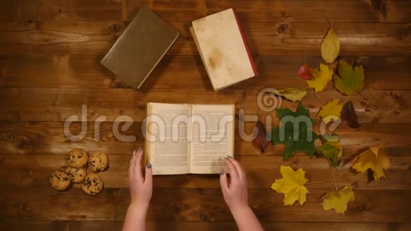 秋季概念俯视图书枫叶烤旧的木桌女人翻阅书页视频的预览图